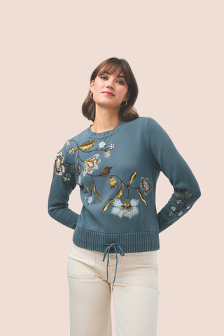 Woman wearing a blue sweater with floral embroidery on a beige background