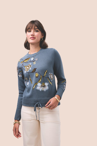 Woman wearing a blue sweater with floral patterns on a beige background